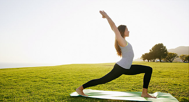 Someone in athletic clothing doing a yoga pose while standing on a yoga mat in a grassy field