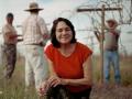 Delores Huerta smiling while kneeling in a field with three people in the background
