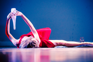 dancer in red dress holding glass bottle while laying on the stage