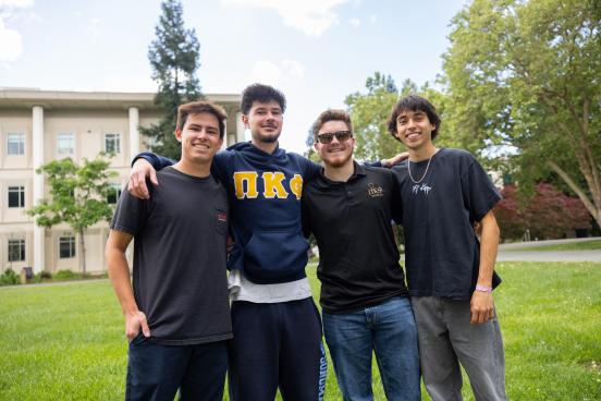 Four students smiling and wearing Phi Kappa Fraternity shirts 