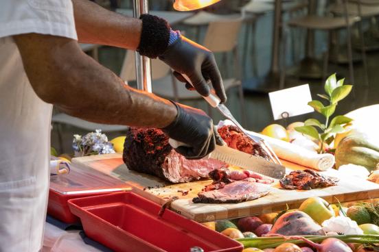 Chef cuts a large meat dish next to a platter of roasted veggies