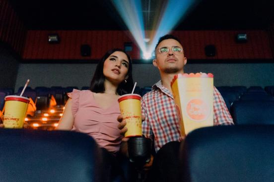 Two people watch a movie with popcorn