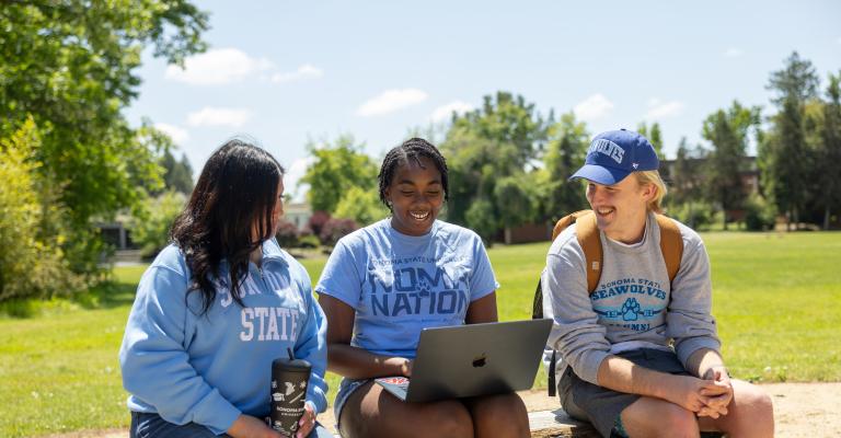 Three students sitting outside looking at a computer