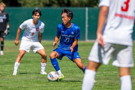 Two soccer players with one kicking a ball and one behind them as an opponent 