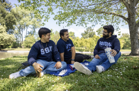 Three students laugh and talk by the lakes