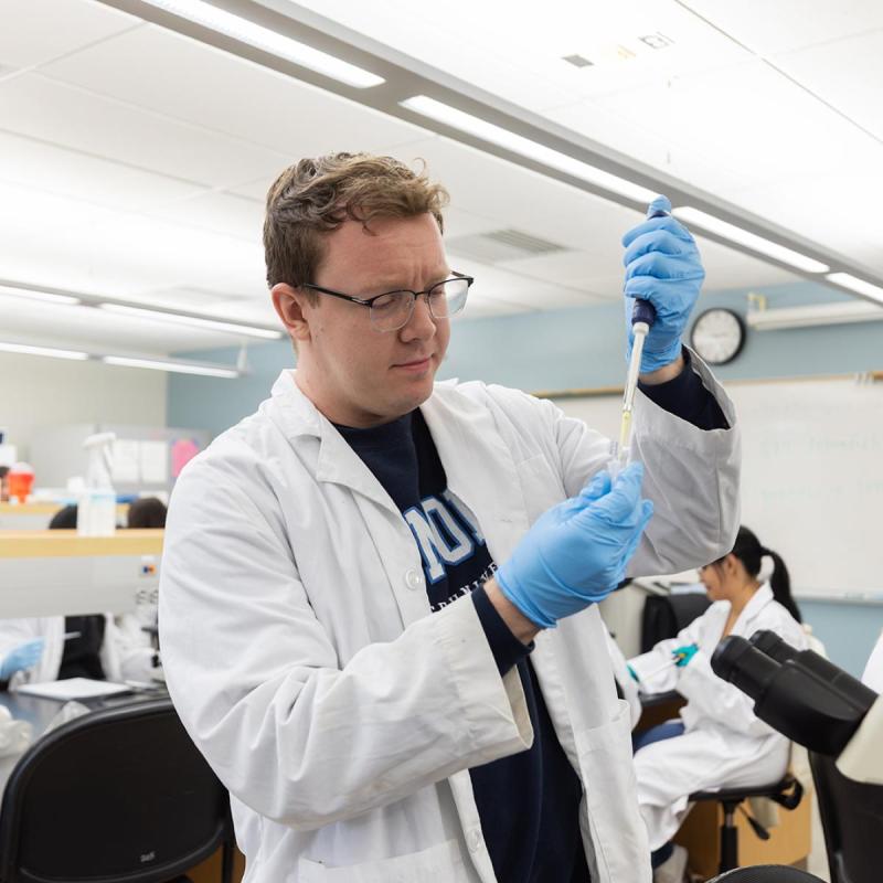 Student in a lab wearing gloves with a serenge 