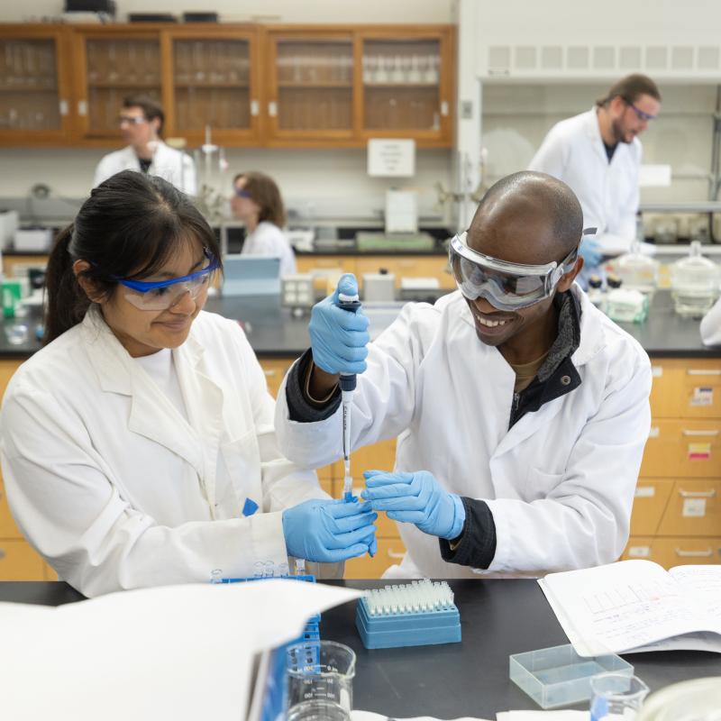 Two students in a lab wearing lab coats and working on a hands on science experiment
