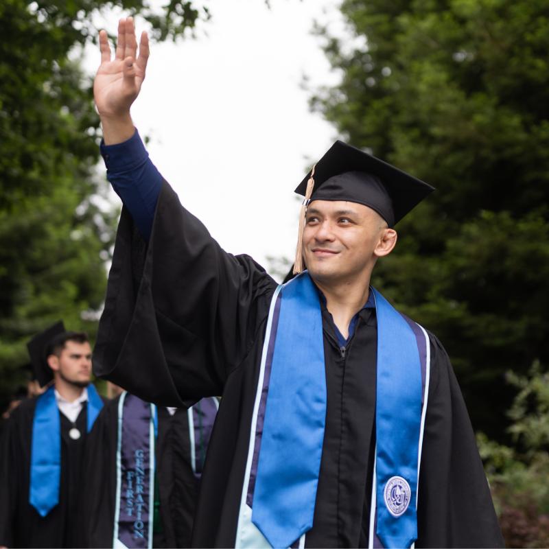 Student wearing regalia at Commencement and waving