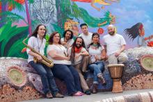 The seven members of Lior Ben Hur smiling and posing with their instruments in front of a colorful mural