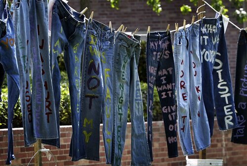 Multiple pairs of denim pants with writing on them hanging from a clothes line