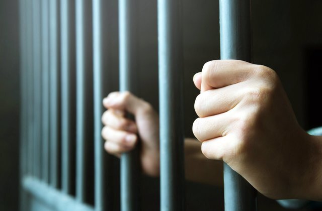 Two hands holding onto the bars of a dimly lit jail cell