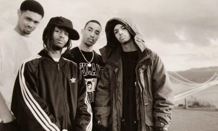 A black and white portrait of the hip hop group The Souls of Mischief standing together in an outdoor setting