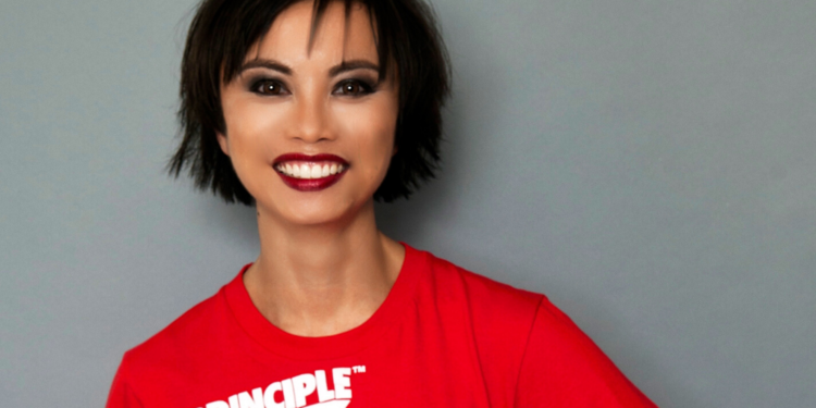 A portrait of Amazin LeThi smiling in a red t-shirt in front of a grey background