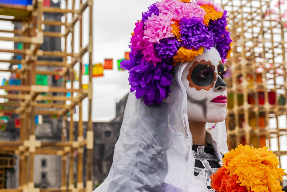 a person wearing skull makeup and a flower headband while carrying a bouquet of flowers