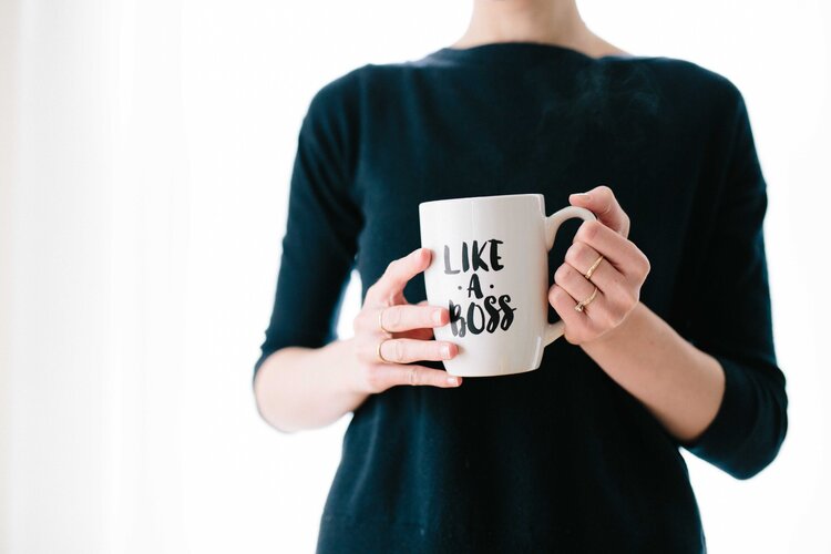 Someone in a black top holding a drinking mug that reads "Like a Boss" 