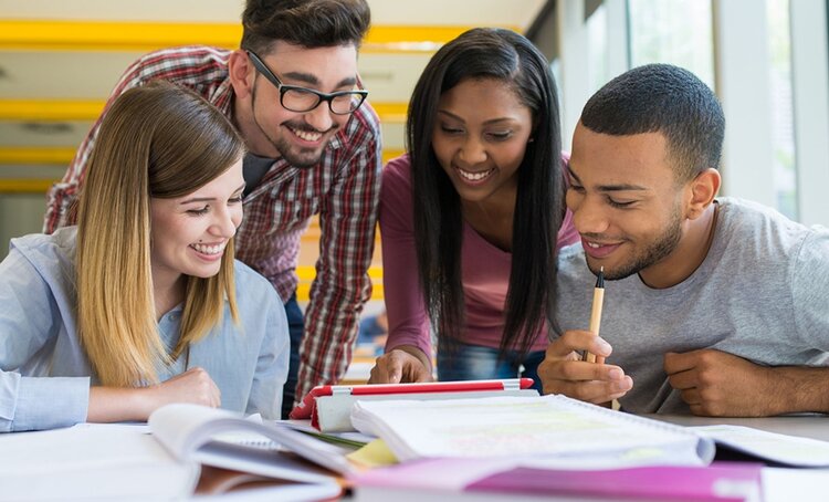 A group of four students smiling while looking at a table full of papers, book, and folders