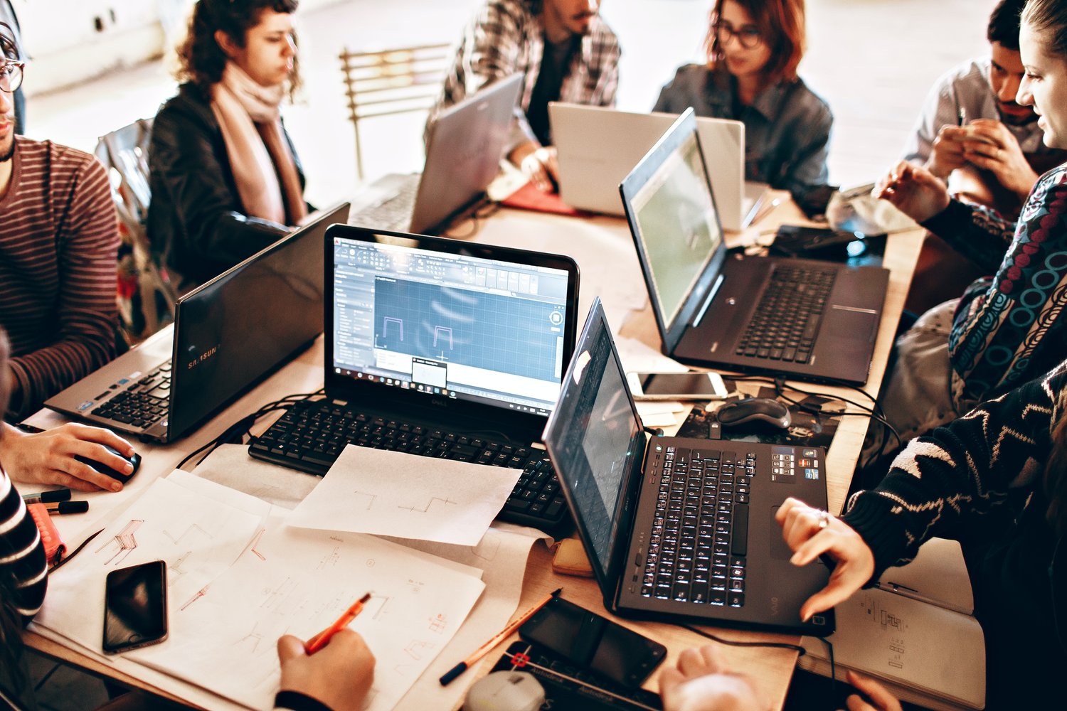 group of people sitting around a table on their laptops