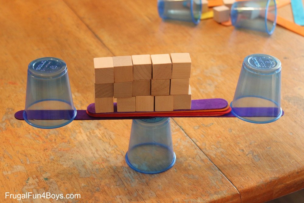 A balanced stack of plastic cups, wooden popsicle sticks, and wood cubes