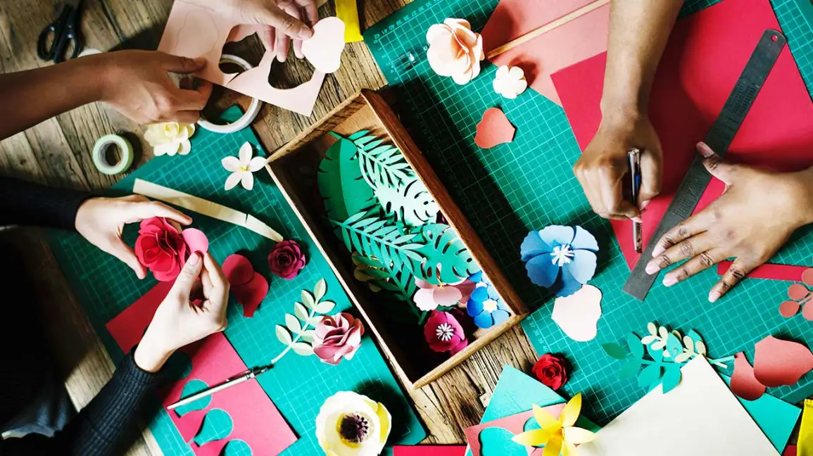 An above-view of multiple people crafting with colorful paper and other crafting materials