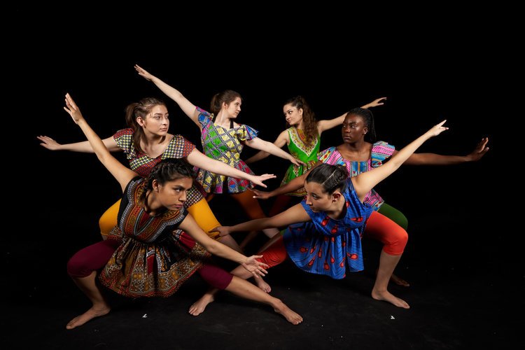 A group of five dancers posing in colorful clothing