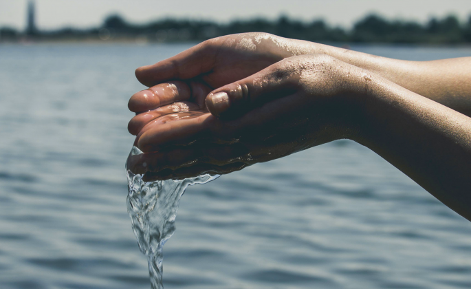 Two cupped hands letting water pour from them with a body of water in the background