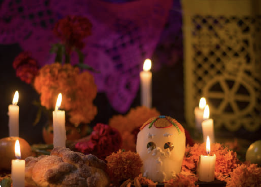 a sugar skull, multiple candles, and multiple orange marigold flowers for Día de los Muertos