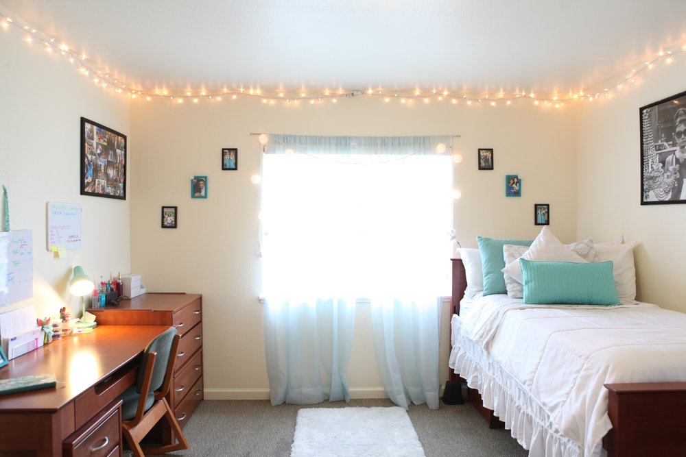A dorm room with photos, string lights, and posters hanging on the walls