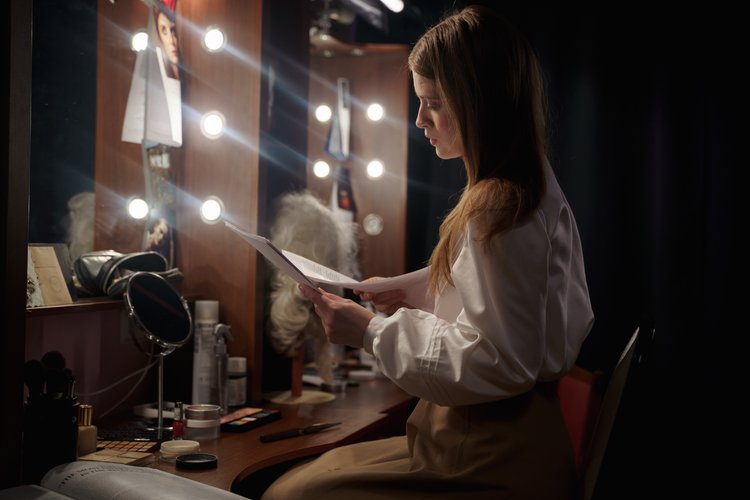 a woman getting ready while reading a script in a dressing room