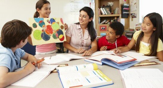 A young student showing their colorful artwork to a group of other smiling students and a teacher 