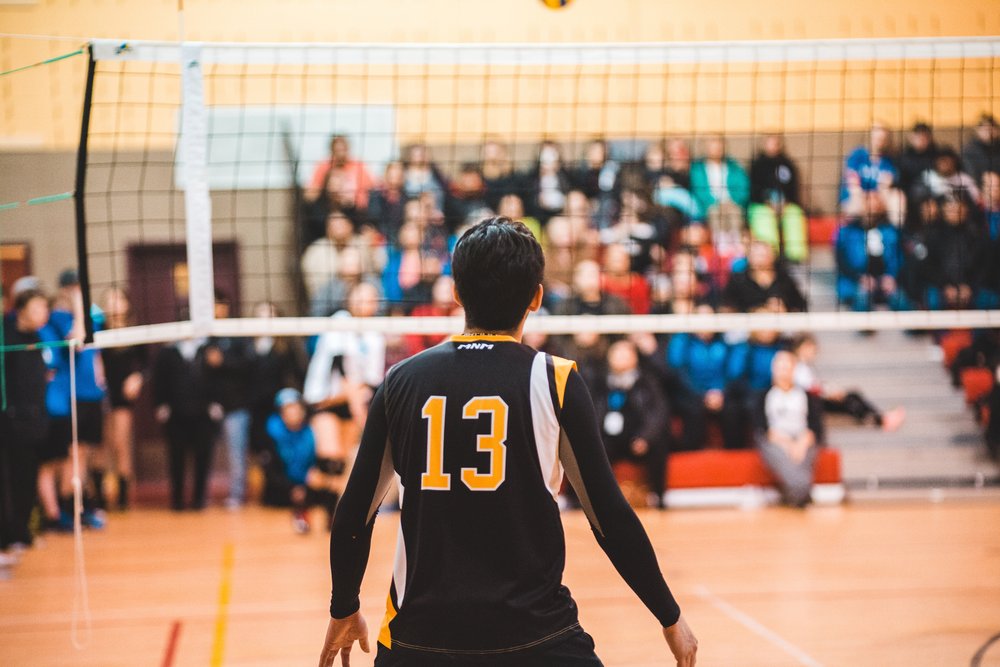 The back of someone wearing a jersey while playing volleyball indoors