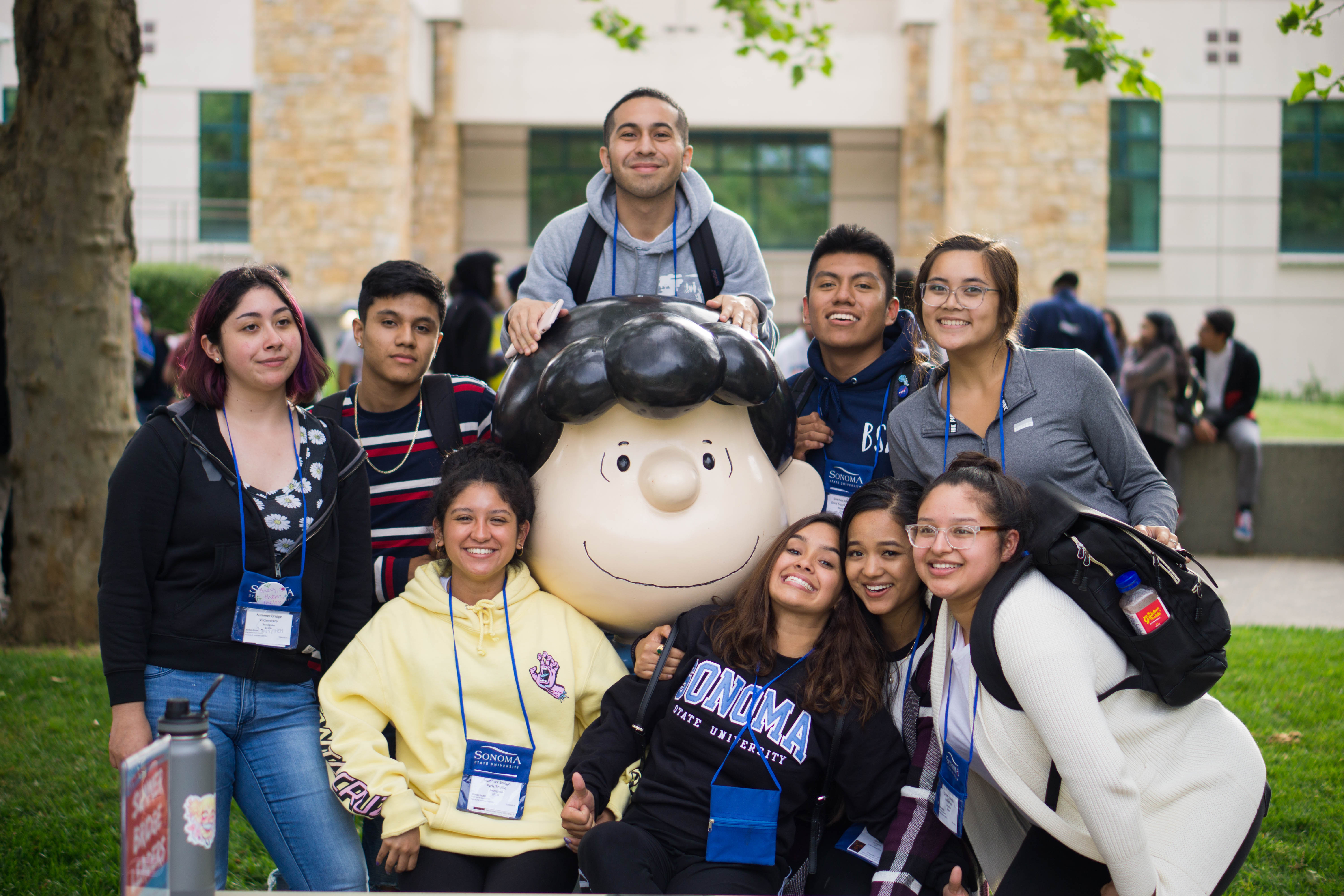 A group of smiling students with lanyards and name tags around their necks while standing around the Lucy statue 