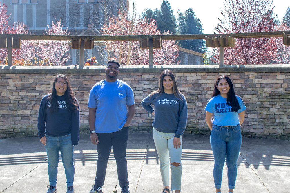 four Sonoma State University students standing in a row in front of the Alumni Amphitheater at Sonoma State University.
