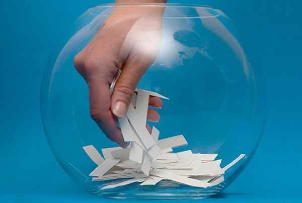 A hand reaching into a fishbowl to pick up a tab of paper 