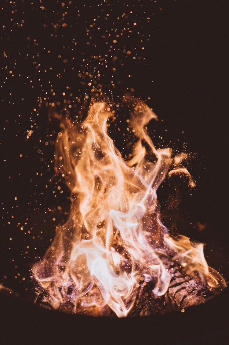 Orange and yellow flames and embers emerging from a fire pit during nighttime 