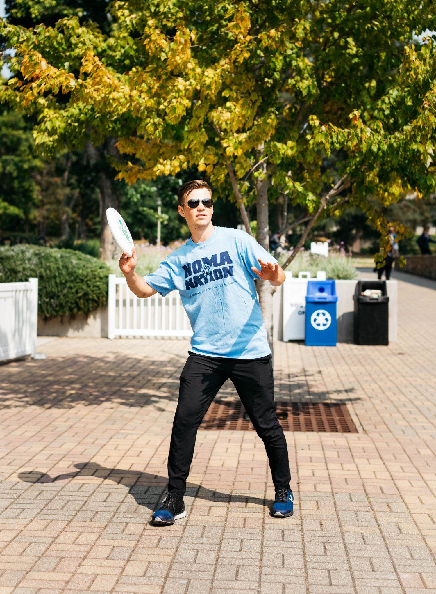 A student wearing a 'Noma Nation' t-shirt throwing a frisbee