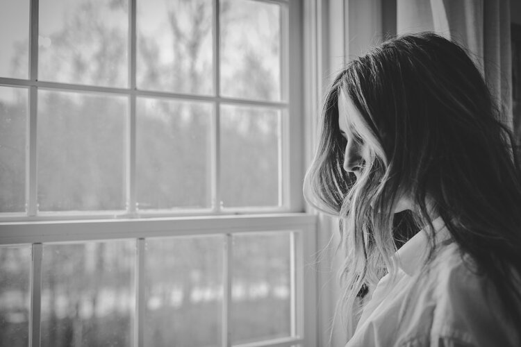 Black and white image of a person with long hair standing in front of a multi-paned window