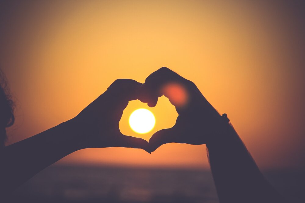 Silhouette of two hands coming together to form the shape of a heart with the sunset in the background