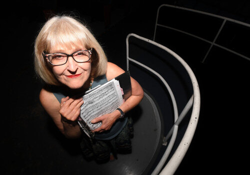 Portrait of Harriet Bennish wearing eyeglasses and holding papers to her chest while smiling