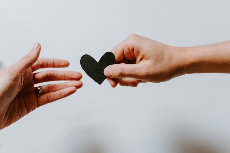 Hand passing a small black heart made of cut paper to another person's hand