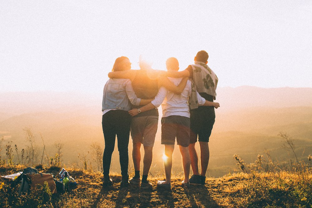 A group of four people hugging in front of the sunset