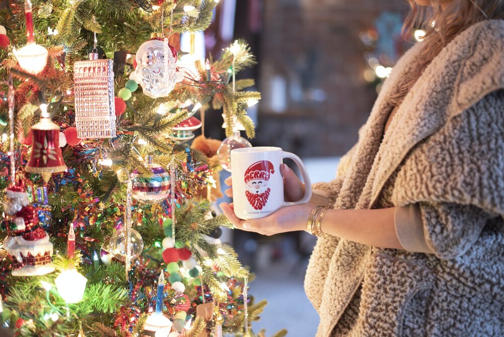 a person holding a coffee mug next to a decorated Christmas tree