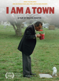 The film poster for 'I Am A Town' featuring a person in a suit smelling potted flowers while standing in a cemetery