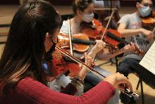 People playing violins while wearing masks in an indoor setting