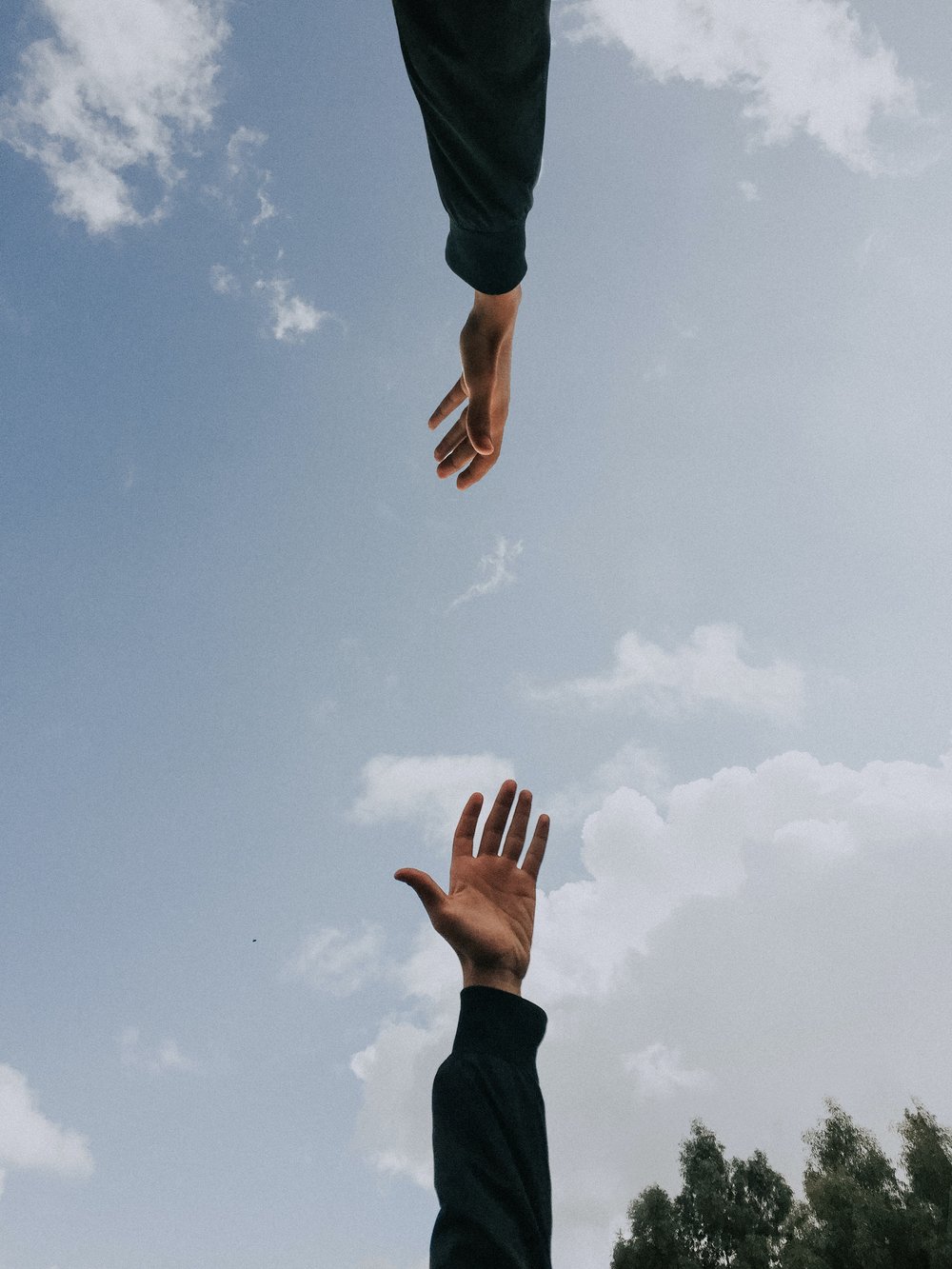 two hands reaching toward each other with the blue sky and white puffy clouds in the background