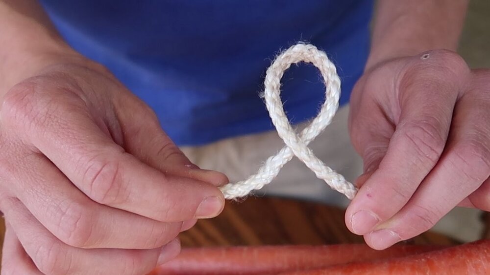 Two hands tying a white rope into a single loop