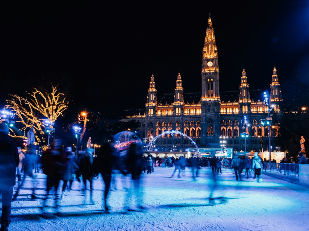 People ice skating outdoors at night with colorful lights surrounding them