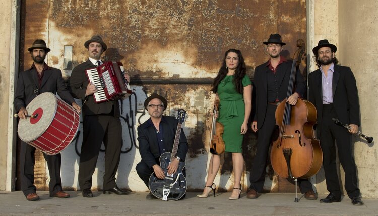 Portrait of the six band members of Kugelplex posing with their instruments in an urban setting