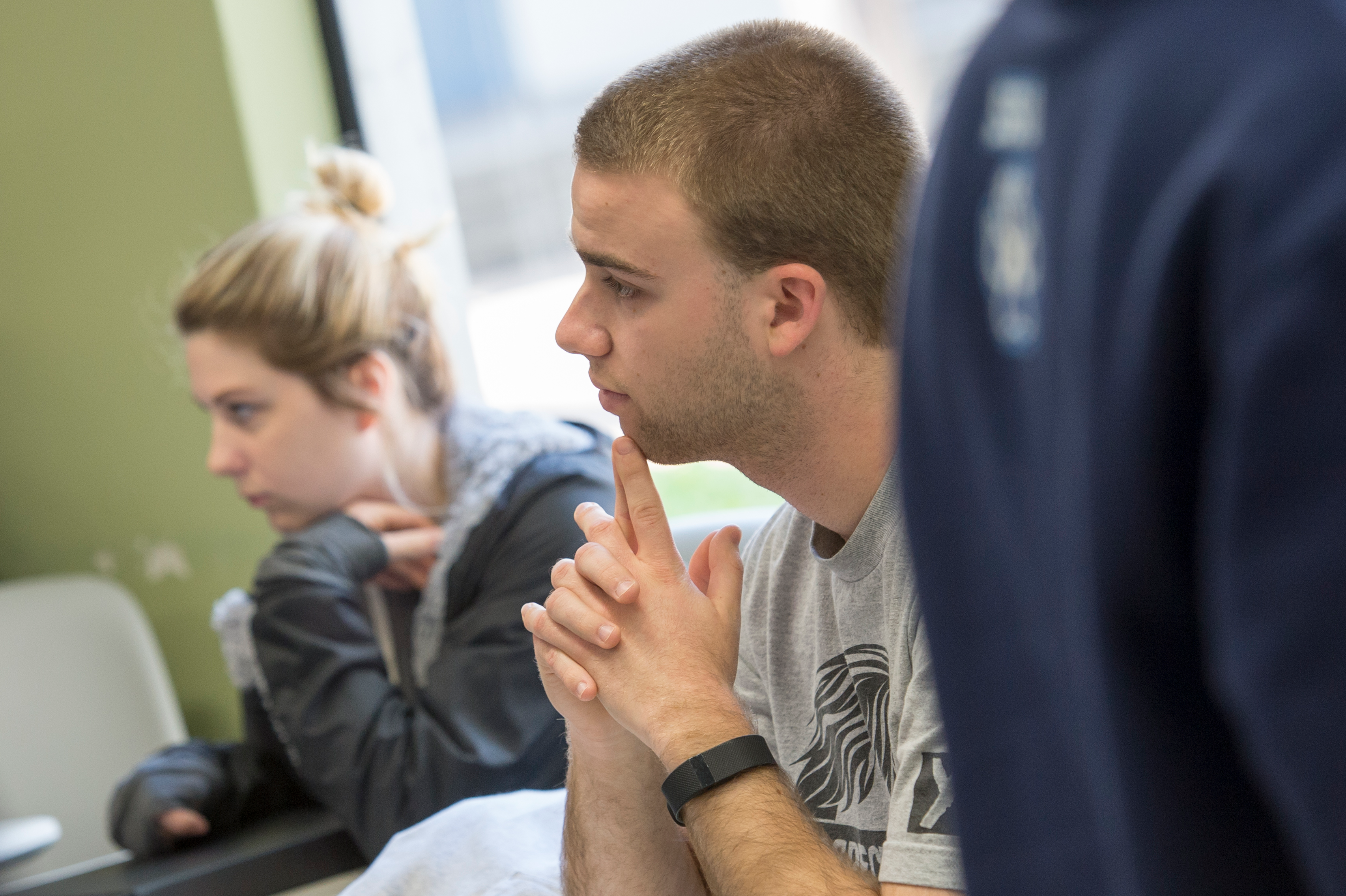 Student seated with elbows on table and clasped fingers on chin listens