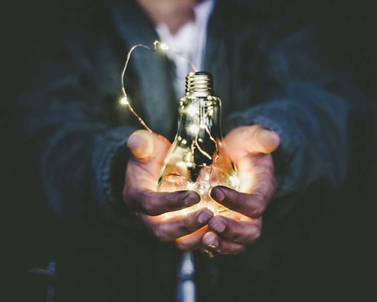 Someone holding a lightbulb with string lights inside of it 