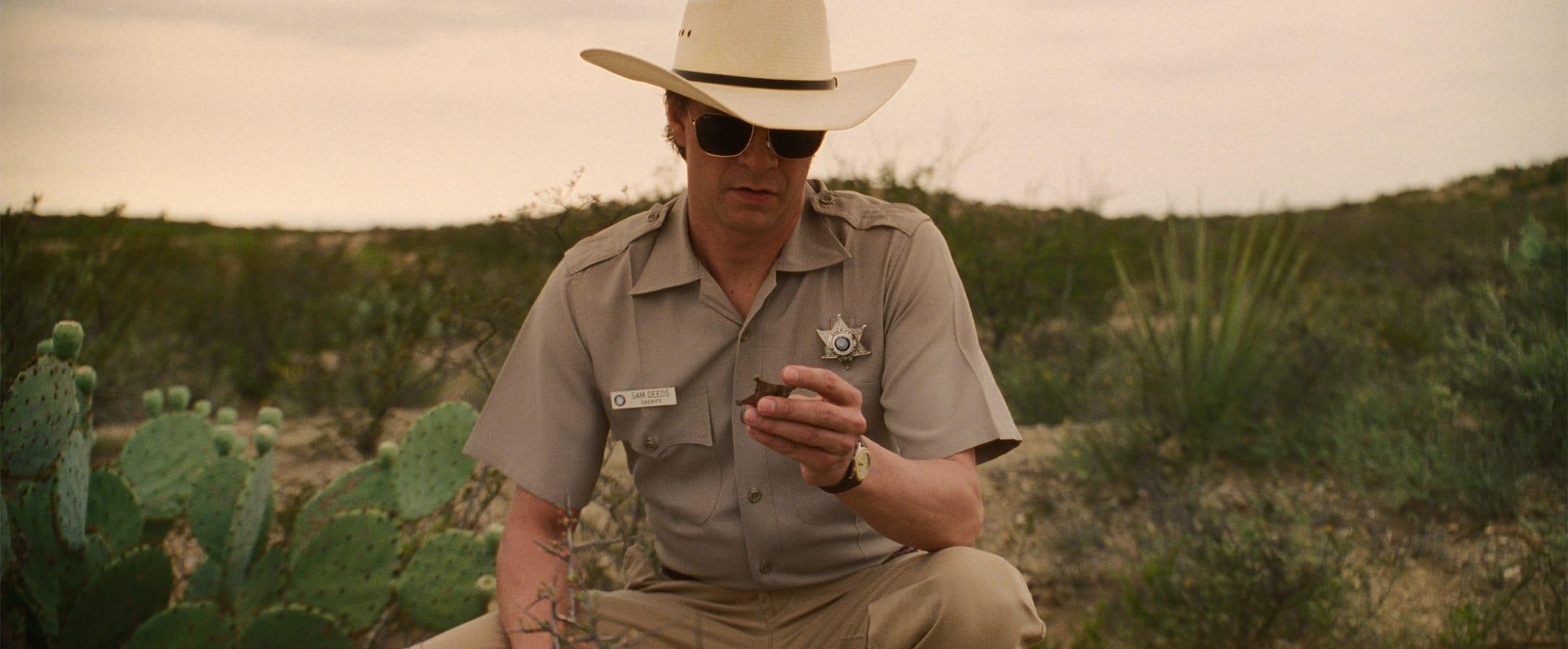 A person in western sheriff gear holding and looking at a star-shaped badge